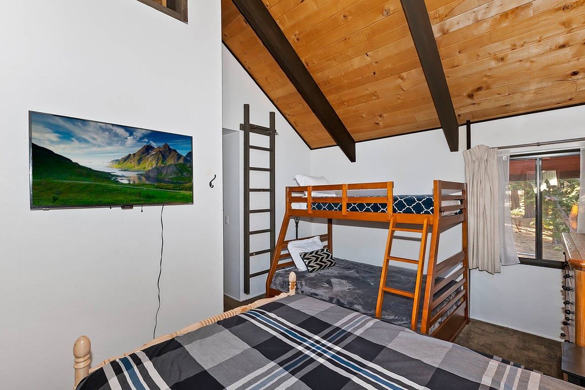 Una habitación con una cama litera, una escalera, un televisor montado en la pared y una ventana con cortinas.