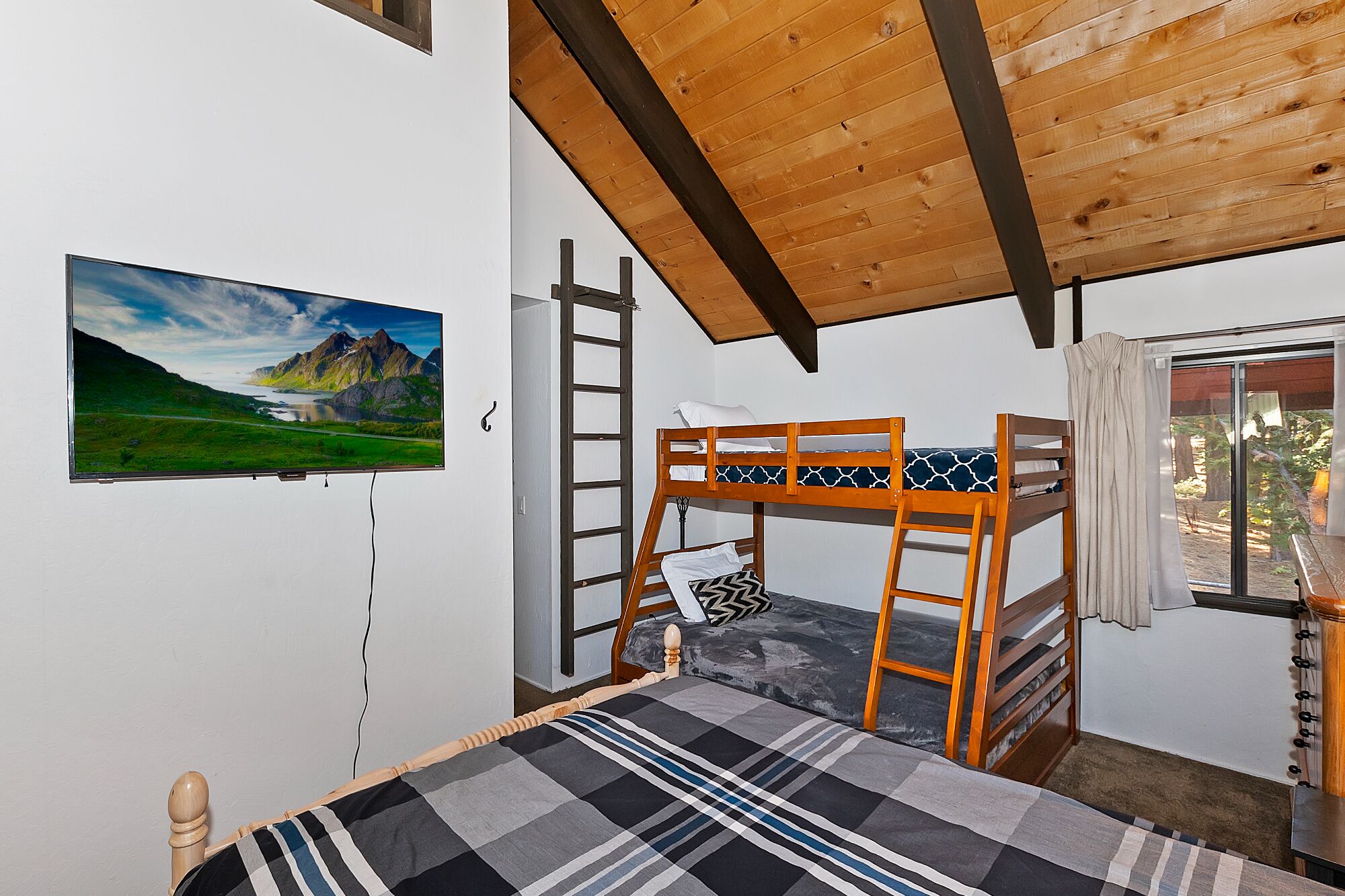 Une chambre avec un lit superposé, un plafond en bois, un tableau représentant un paysage et une fenêtre avec des rideaux.