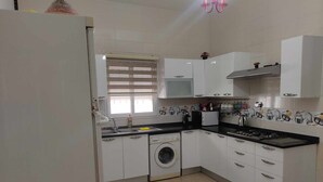 Een moderne keuken met witte kasten, een ingebouwde wasmachine, een gasfornuis en een raam met jaloezieën.