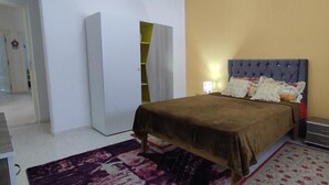 Een slaapkamer met een bed, een kledingkast, een nachtkastje en een kamerkleed met dessin.