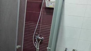 Un espace douche doté d’une porte en verre, d’un lavabo blanc avec un miroir et d’un tapis de bain rouge.