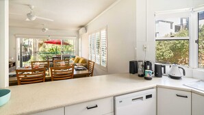A kitchen with white cabinets, a dishwasher, a coffee maker, and a red umbrella outside. - Sunny Seaside Retreat in Coolum Beach (Coolum Region)