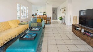 A living room with a sofa, coffee table, TV, and a dining area in the background. - Sunny Seaside Retreat in Coolum Beach (Coolum Region)