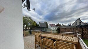 Eine Holzterrasse mit Tisch und Stühlen, eine Satellitenschüssel und im Hintergrund Häuser und Bäume.