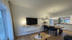 Ein modernes Wohnzimmer mit Fernseher, Essbereich und Küche.