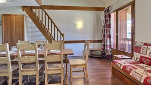 A dining area with wooden chairs and a table set for four, a wooden staircase, and a bed with a patterned quilt. - Spacious duplex for 5 at the foot of the slopes (Plagne Soleil)