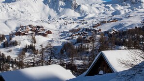 A snow-covered mountain village with wooden chalets and a ski slope. - Spacious duplex for 5 at the foot of the slopes (Plagne Soleil)