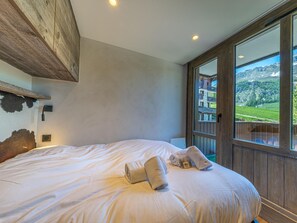Un dormitorio con una cama grande, cabecera de madera, ventana con vista a las montañas y techo de madera.