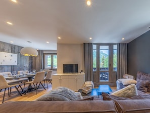 A modern living room with a dining area, a flat-screen TV, and a balcony with a view of the outdoors.