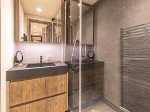 A modern bathroom with a glass-enclosed shower, a wooden vanity, and a large mirror.
