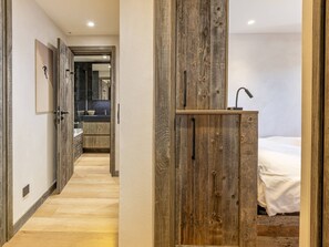 A hallway leading to a bathroom with a wooden door, a sink, and a mirror.
