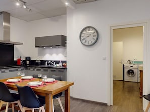 Cozinha moderna com área de refeições, um relógio na parede e uma máquina de lavar ao fundo.