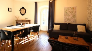 A modern living room with a dining area, featuring a wooden floor, a black sofa, a wooden coffee table, and a dining table with chairs.