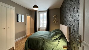 A bedroom with a bed, wardrobe, window, and a wall with a floral pattern.