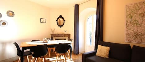 Ein gemütliches Wohnzimmer mit einem dunklen Sofa, einem Esstisch mit Stühlen, einem Kamin und einer Karte an der Wand.