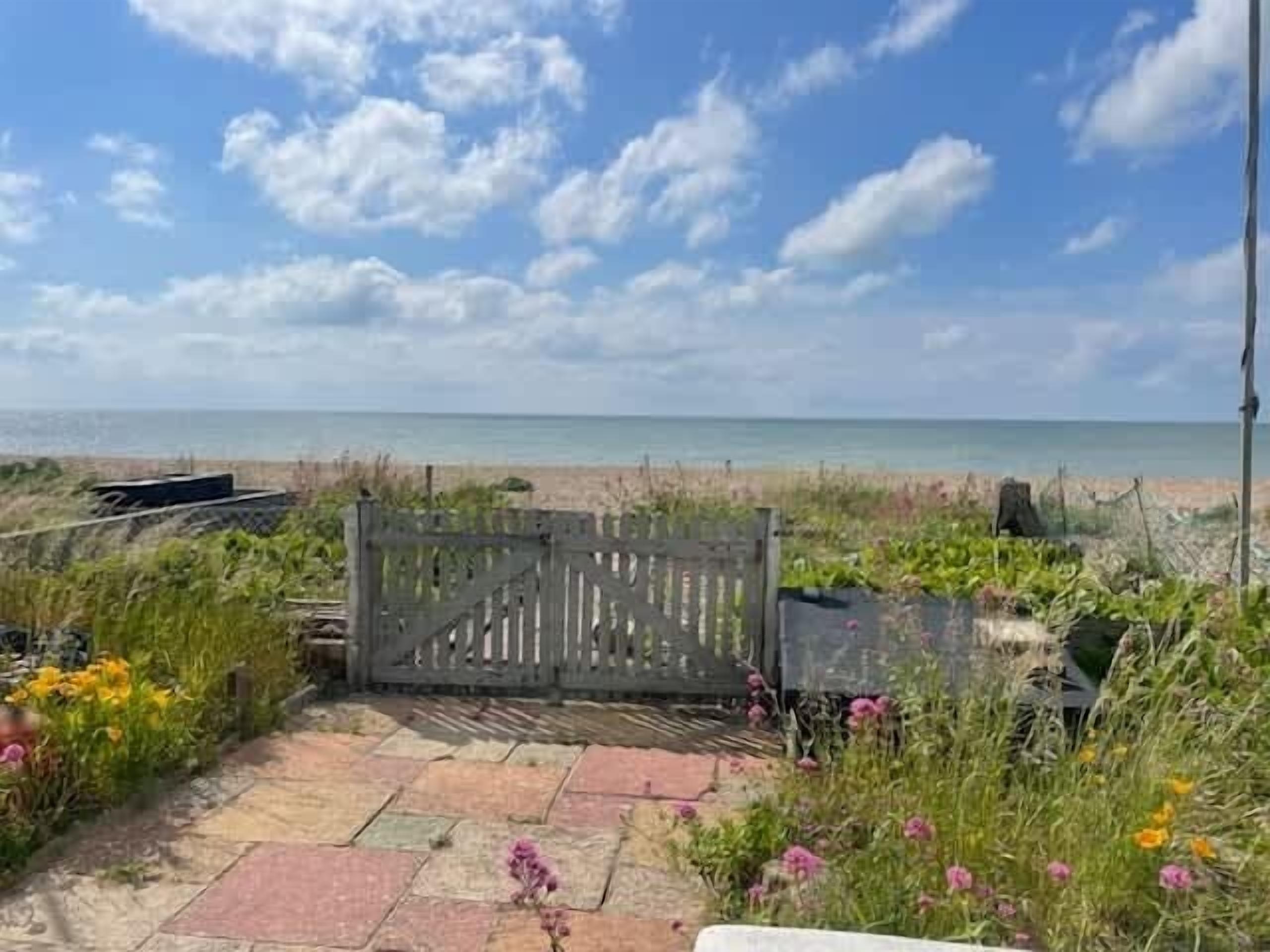 A pathway leading to a beach with a wooden gate, surrounded by various plants and flowers.