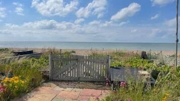 A pathway leading to a beach with a wooden gate, surrounded by various plants and flowers.