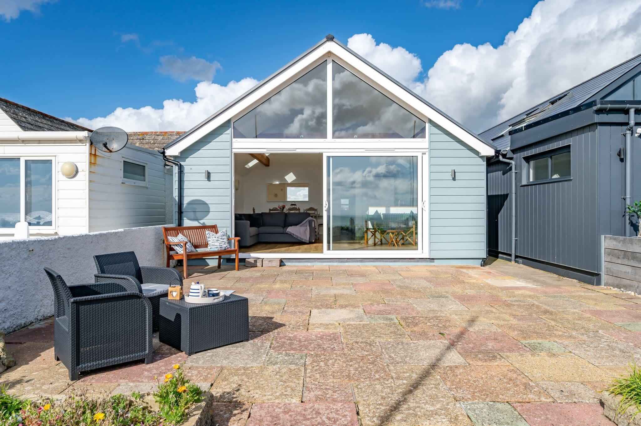A modern house with a patio area featuring outdoor furniture, a sliding glass door leading to an interior space with a sofa and a dining table.