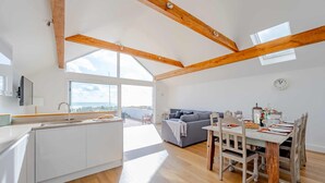 Een moderne keuken met een groot eiland, houten balken, een eethoek met een houten tafel en stoelen, en uitzicht op de stad door grote ramen.