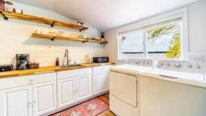 Eine Küche mit weißen Schränken, Holzregalen, einem roten Teppich und einem Fenster mit Blick.