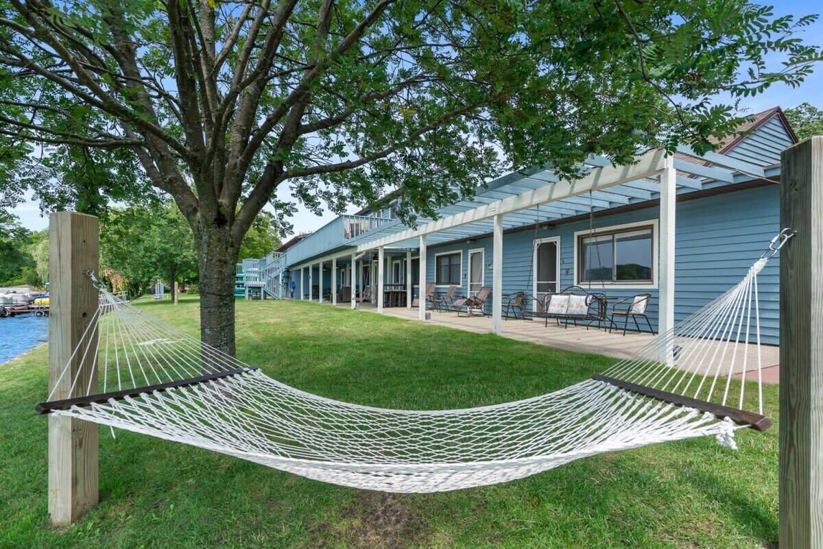A hammock under a tree in a backyard with a house and patio furniture.