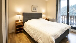 A bedroom with a large bed, two bedside tables with lamps, a radiator, and a window with a view of a forested area. - Spacious chalet for 8, close to center and lifts (Châtel)