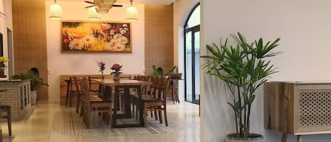 A spacious dining area with a wooden table and chairs, a large painting on the wall, and a potted plant.