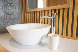 Un lavabo sur colonne blanc, avec un robinet, une tasse blanche et un porte-serviette, le tout posé sur un comptoir.
