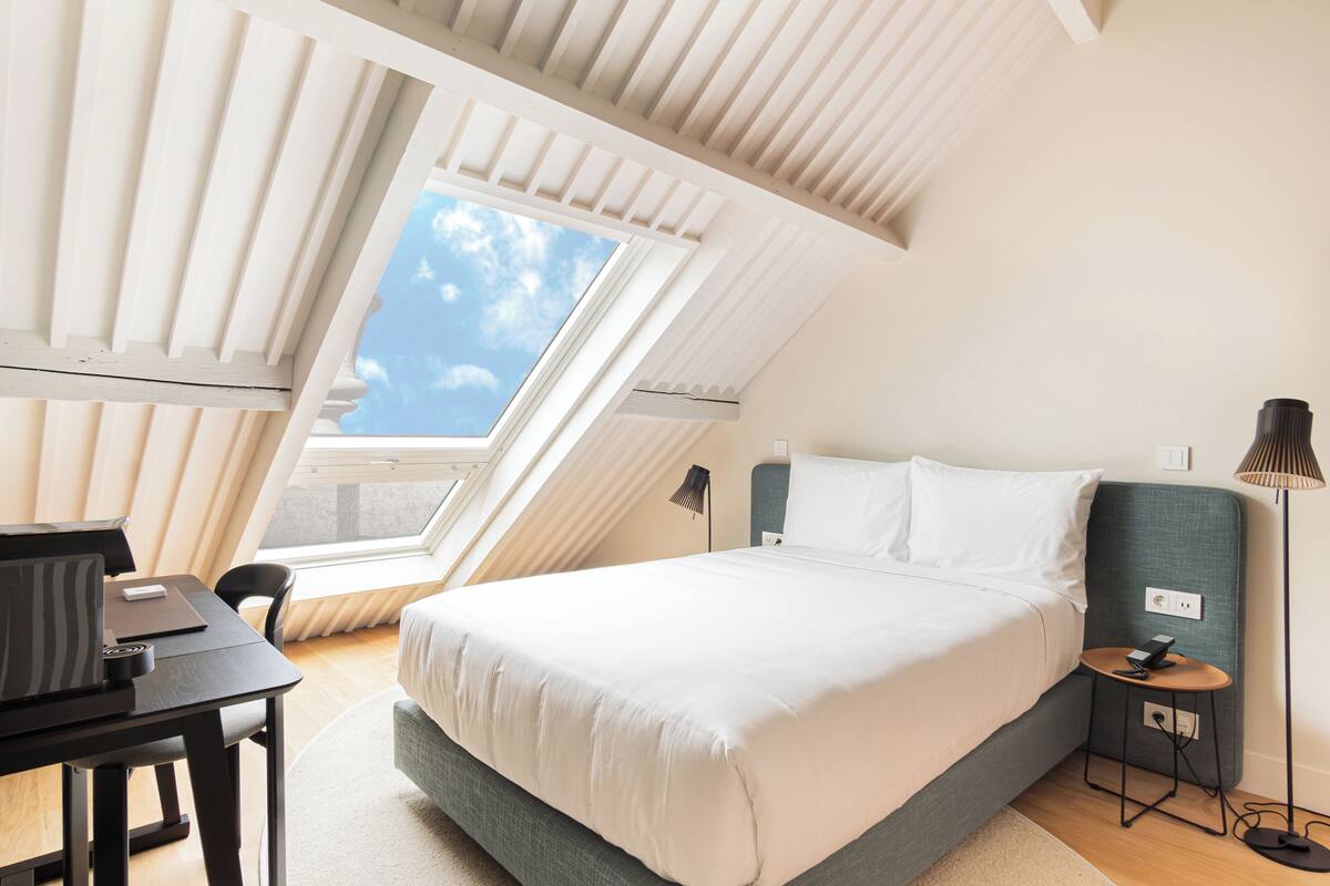 Un dormitorio con cama, escritorio, silla, mesita y lámpara.