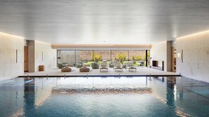 Una piscina interior con diseño moderno, rodeada de zonas de estar y vistas a un jardín.