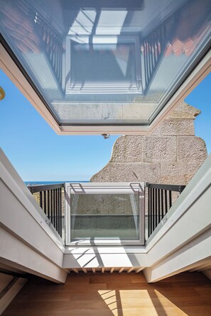 Un balcon moderne doté d’une paroi en verre, d’un plancher en bois et d’un mur en pierre en arrière-plan.