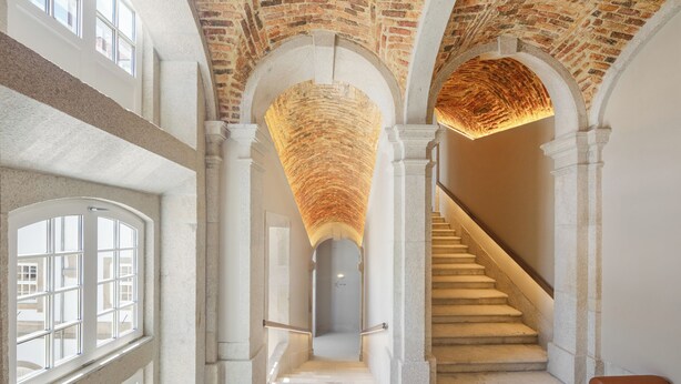 Una imponente escalera con techo de ladrillo y columnas blancas, que conduce a un segundo piso.