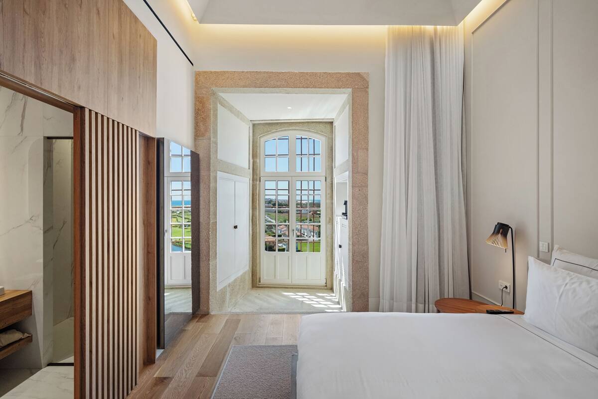 Un dormitorio moderno con una cama grande, una mesita de noche de madera y vistas al exterior a través de un ventanal.