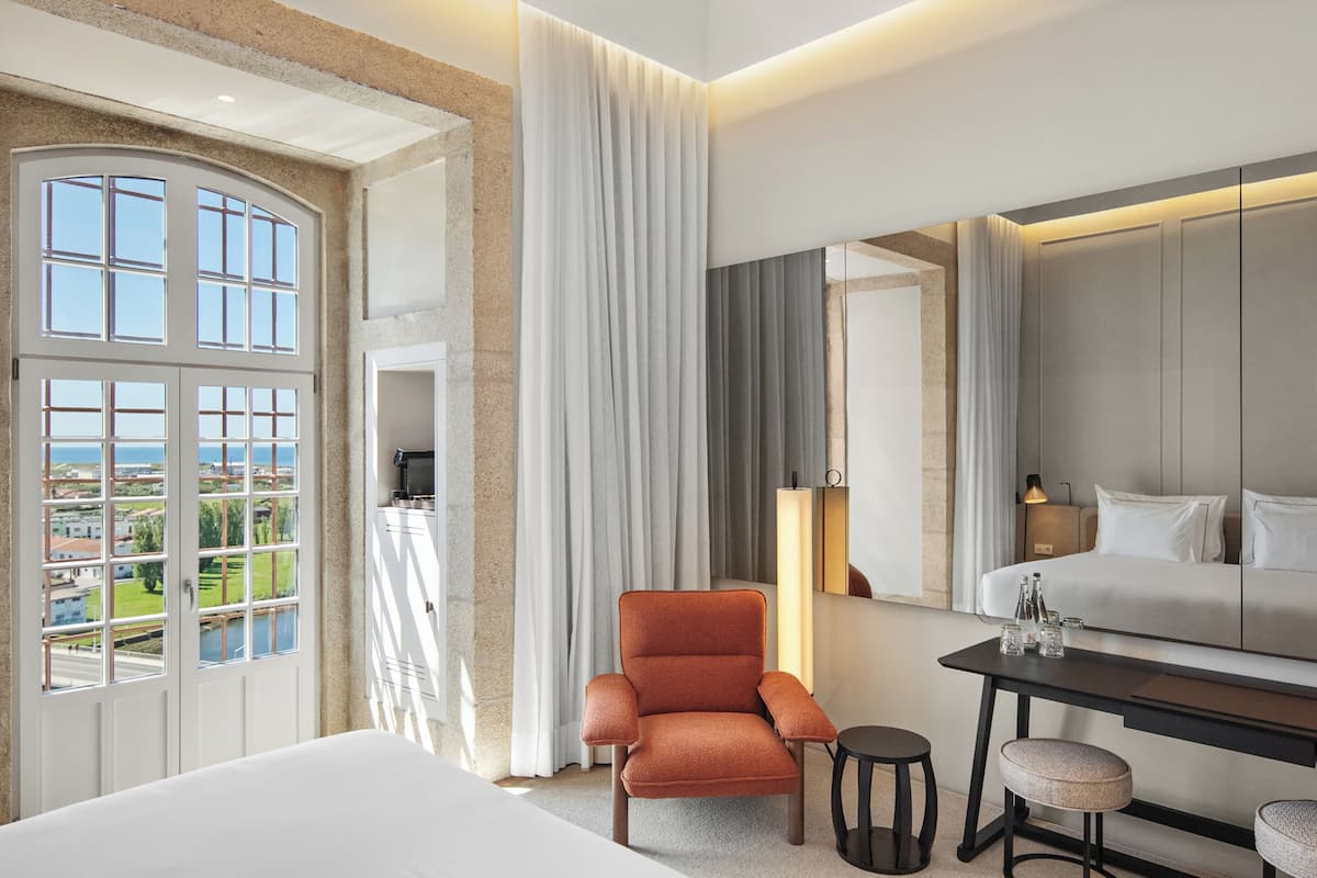 Habitación de hotel con una cama grande, una silla, una mesita y vistas a la ciudad.