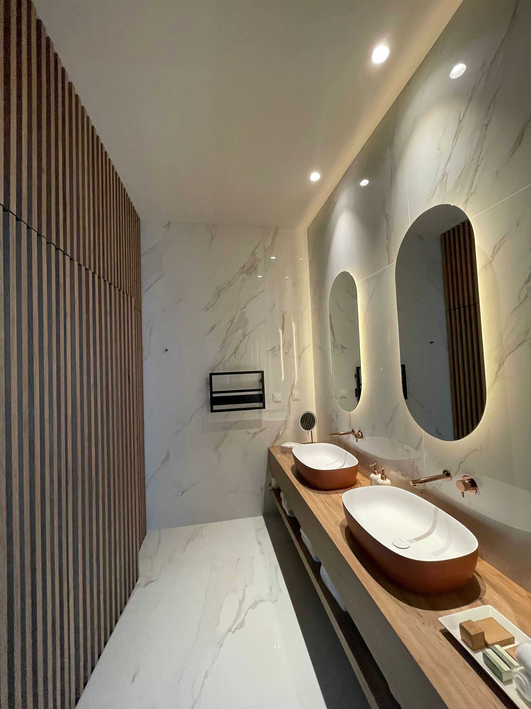 Une salle de bain moderne avec deux vasques, des murs en marbre et un lambris en bois.