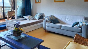 A cozy living room with a sofa, a small table with a plant, and a window with curtains. - Studio Glovettes 35m², Perfect for Ski & Hiking (Villard-de-Lans)