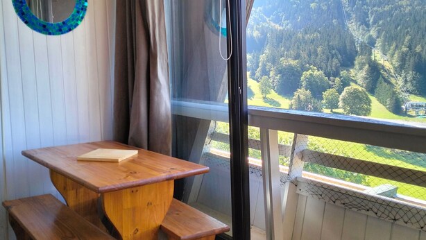 A wooden table with benches, a mirror, and a view of a forested valley through a window. - Studio Glovettes 35m², Perfect for Ski & Hiking (Villard-de-Lans)