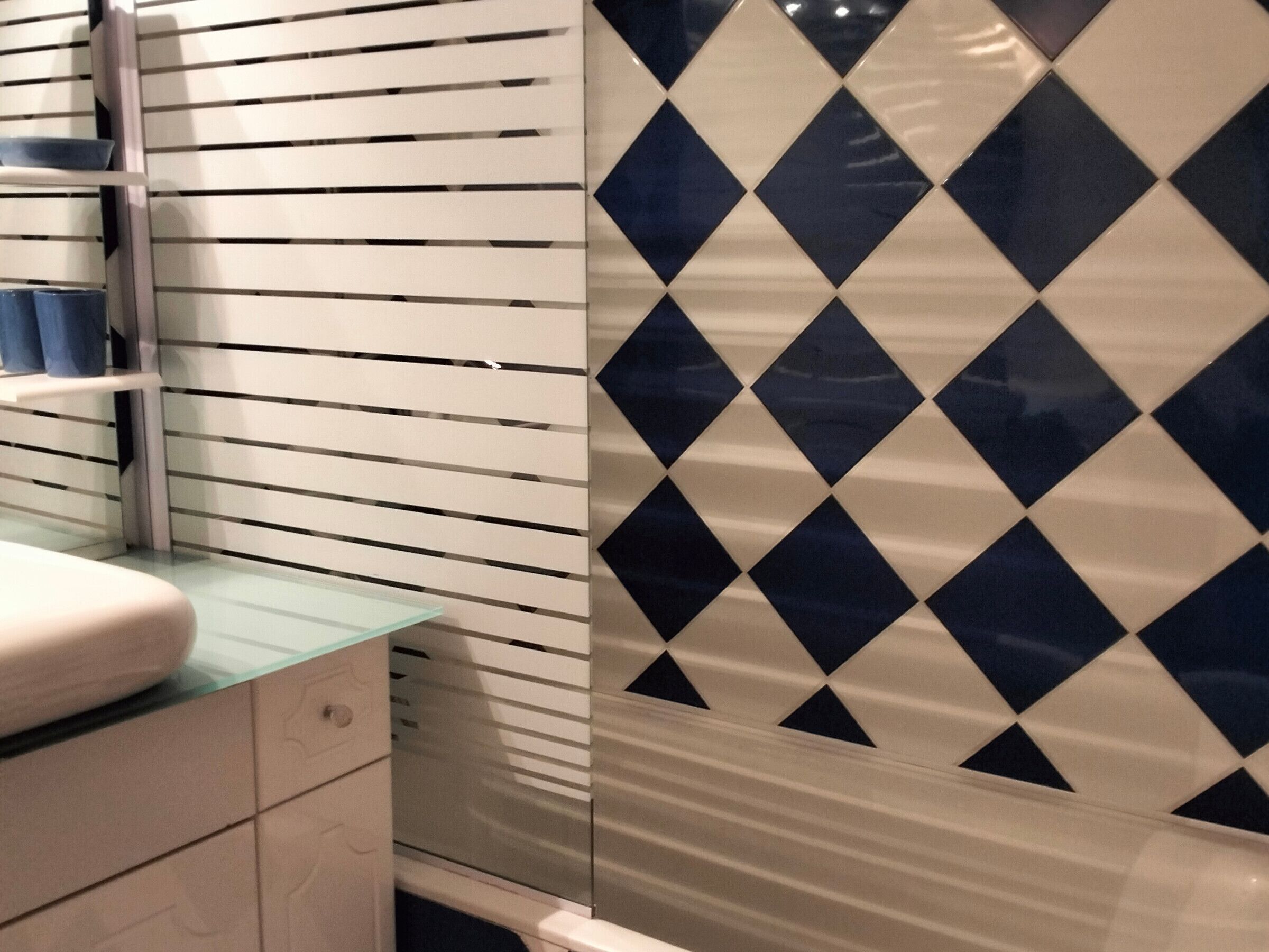 Un baño con un lavabo blanco, una encimera de cristal y una pared con un estampado azul y blanco a cuadros.
