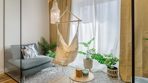 Una sala de estar moderna con un sofá, una silla colgante, un accesorio de luz de macramé y una planta en maceta.