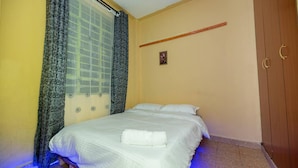 A bedroom with a bed, a wooden wardrobe, a window with curtains, and a small picture on the wall. - Repose Stay - 2br, Wifi, Cctv, Parking in Karen (Nairobi)