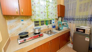 A compact kitchen with wooden cabinets, a gas stove, a microwave, and a small refrigerator. - Repose Stay - 2br, Wifi, Cctv, Parking in Karen (Nairobi)