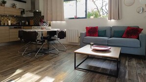 Una cucina moderna con angolo pranzo, un divano grigio con cuscini rossi e una finestra con tende.