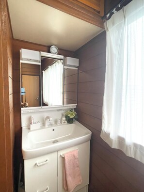 A bathroom with a white sink, a mirror, a clock, and a window with curtains.