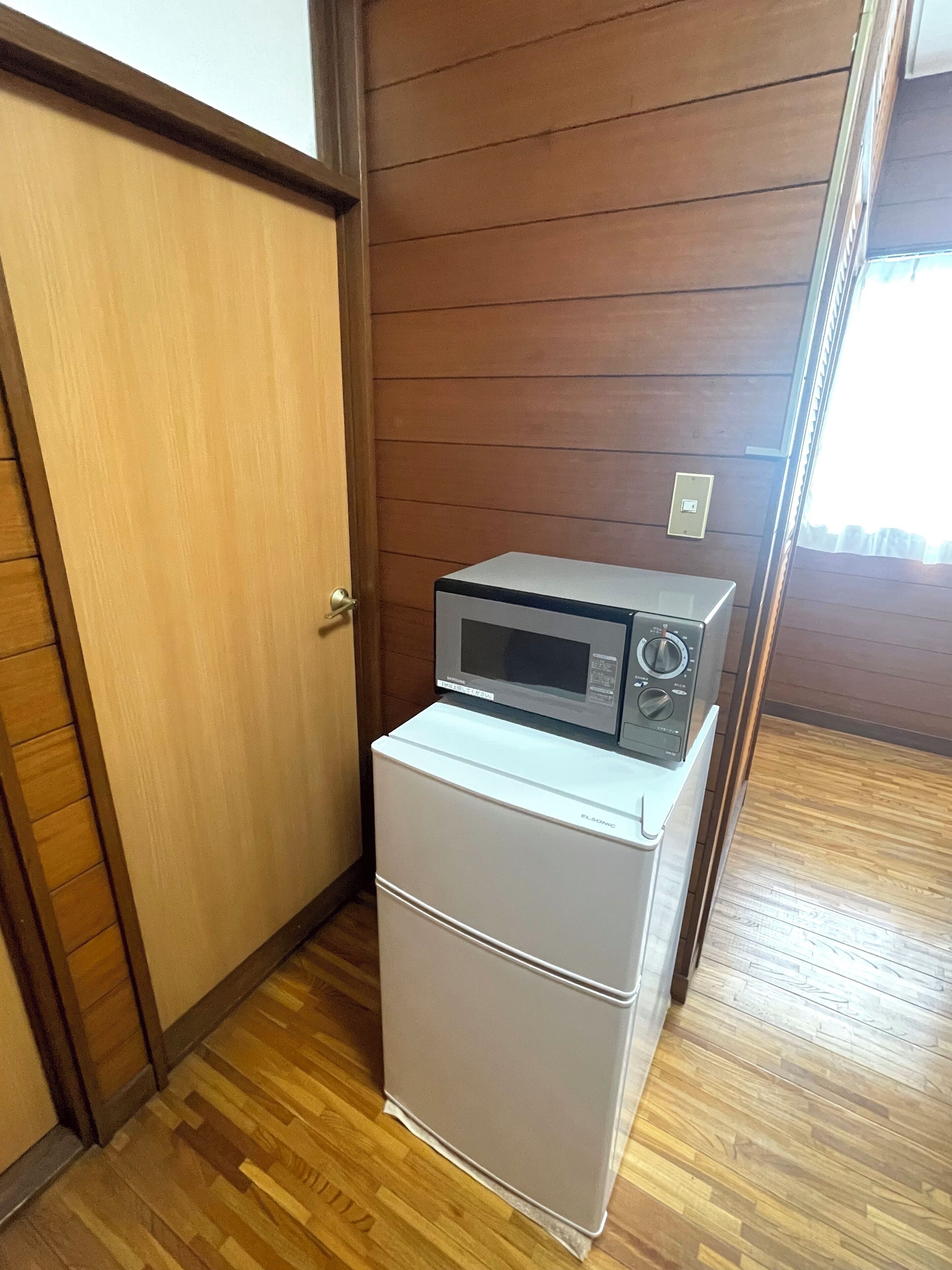 Eine kleine Küche mit Kochnische, Mikrowelle und Kühlschrank in einem Raum mit Holzwandverkleidung und Holzboden.