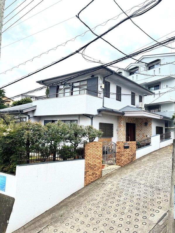 A modern two-story house with a balcony, a brick entrance, and a gated driveway.