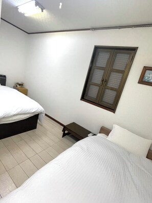 A bedroom with two beds, a small bedside table, a nightstand, a window, and a ceiling light fixture.