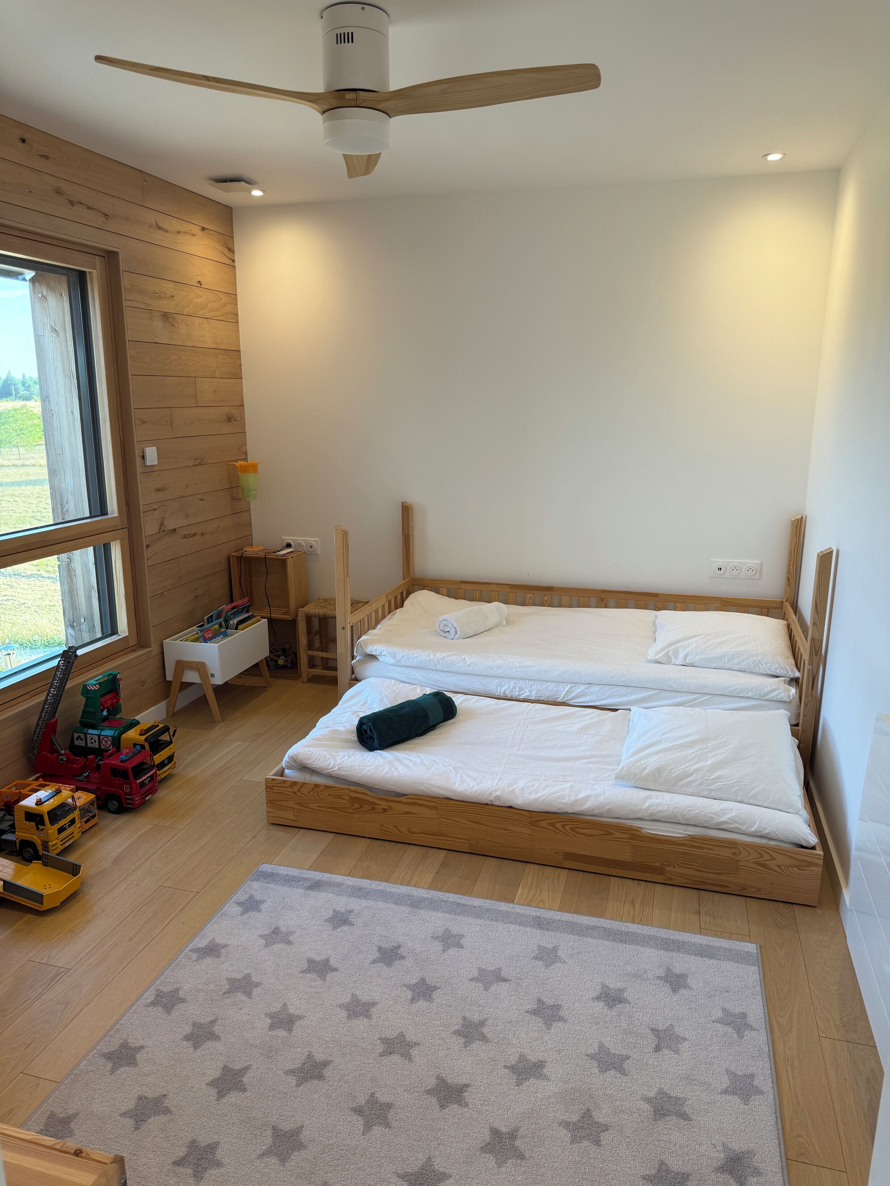 A bedroom with two wooden beds, a ceiling fan, a window, and a star-patterned rug.