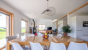 Un espace repas moderne avec une grande table en bois, des chaises blanches et un grand saladier à fruits placé au centre.