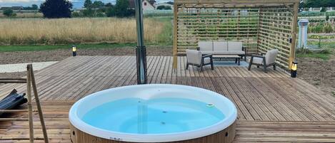 A hot tub on a wooden deck with a pergola and outdoor furniture.