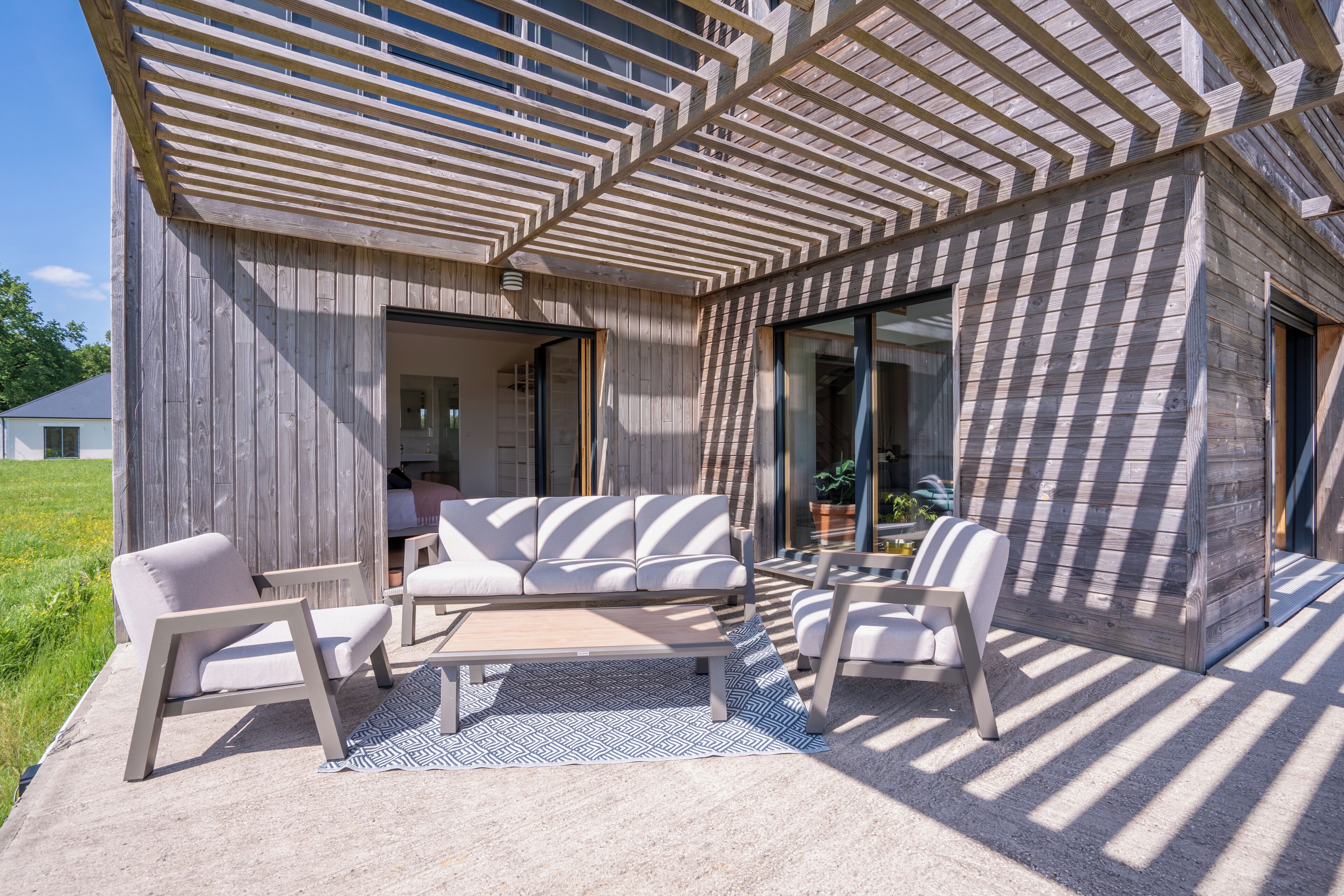 Ein zeitgemäßer Außenbereich mit einer Holzpergola, einem Sofa und zwei Sesseln.